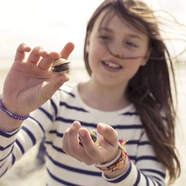 Young girl in a sailor suit holding a shell in her hand to check the size.